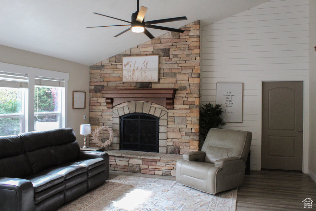 Living room featuring a stone fireplace, wood-type flooring, ceiling fan, and vaulted ceiling