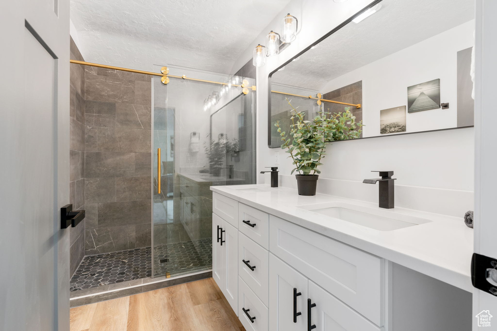 Bathroom with a shower with door, wood-type flooring, oversized vanity, and double sink