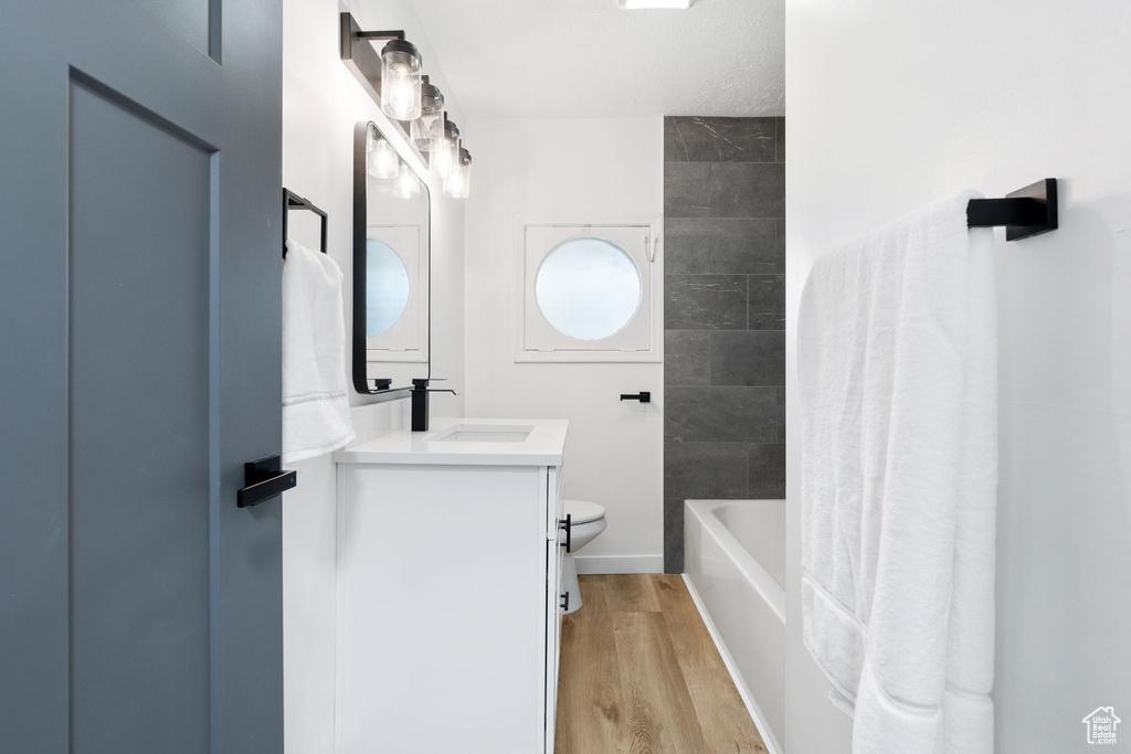 Full bathroom with hardwood / wood-style floors, tiled shower / bath, vanity, and toilet