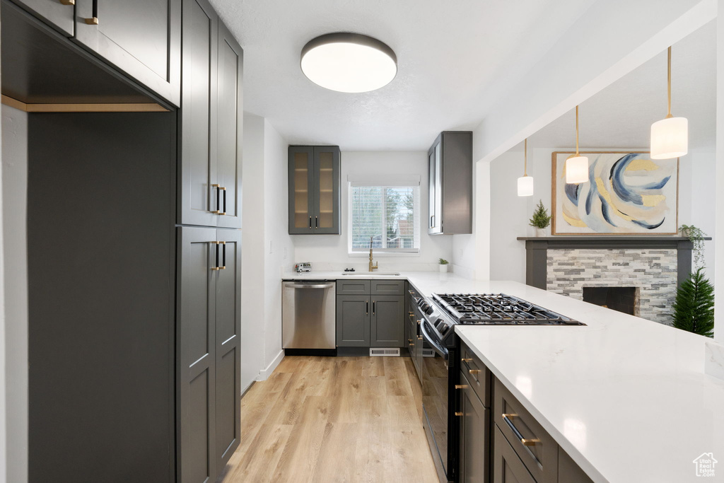 Kitchen with a stone fireplace, sink, gas range oven, light hardwood / wood-style floors, and stainless steel dishwasher