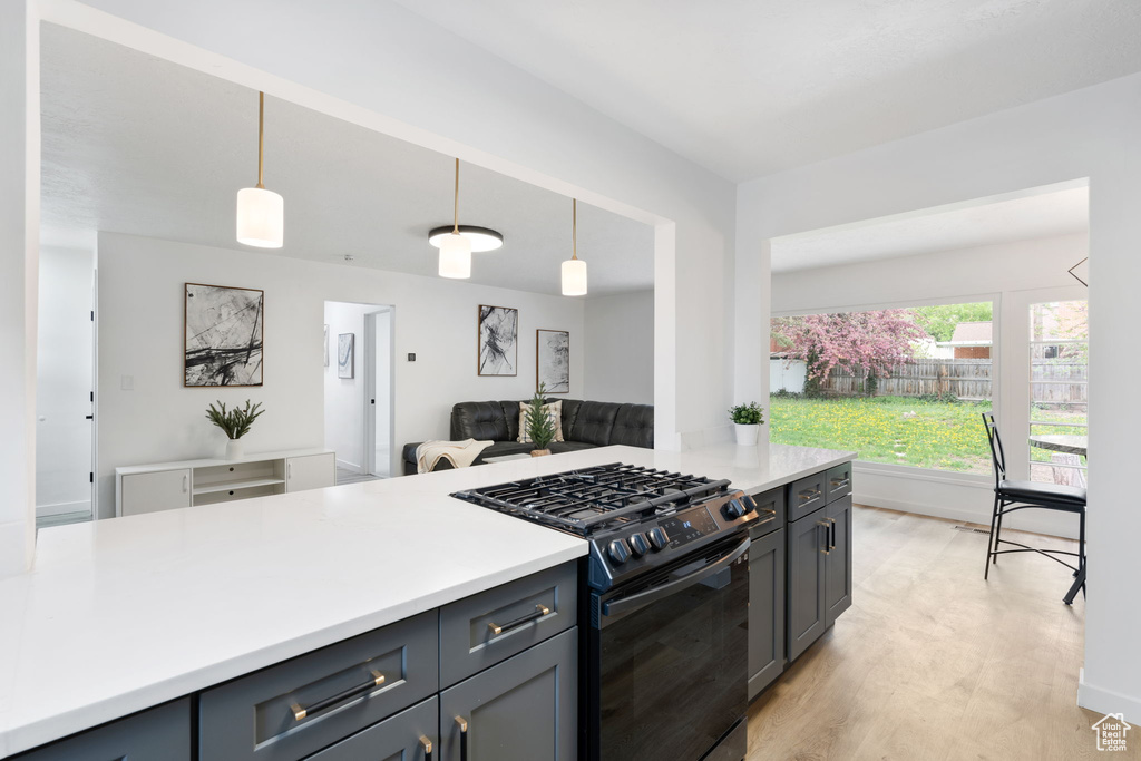 Kitchen featuring decorative light fixtures, black gas range oven, and light wood-type flooring