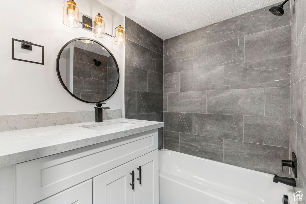 Bathroom featuring a textured ceiling, vanity, and tiled shower / bath