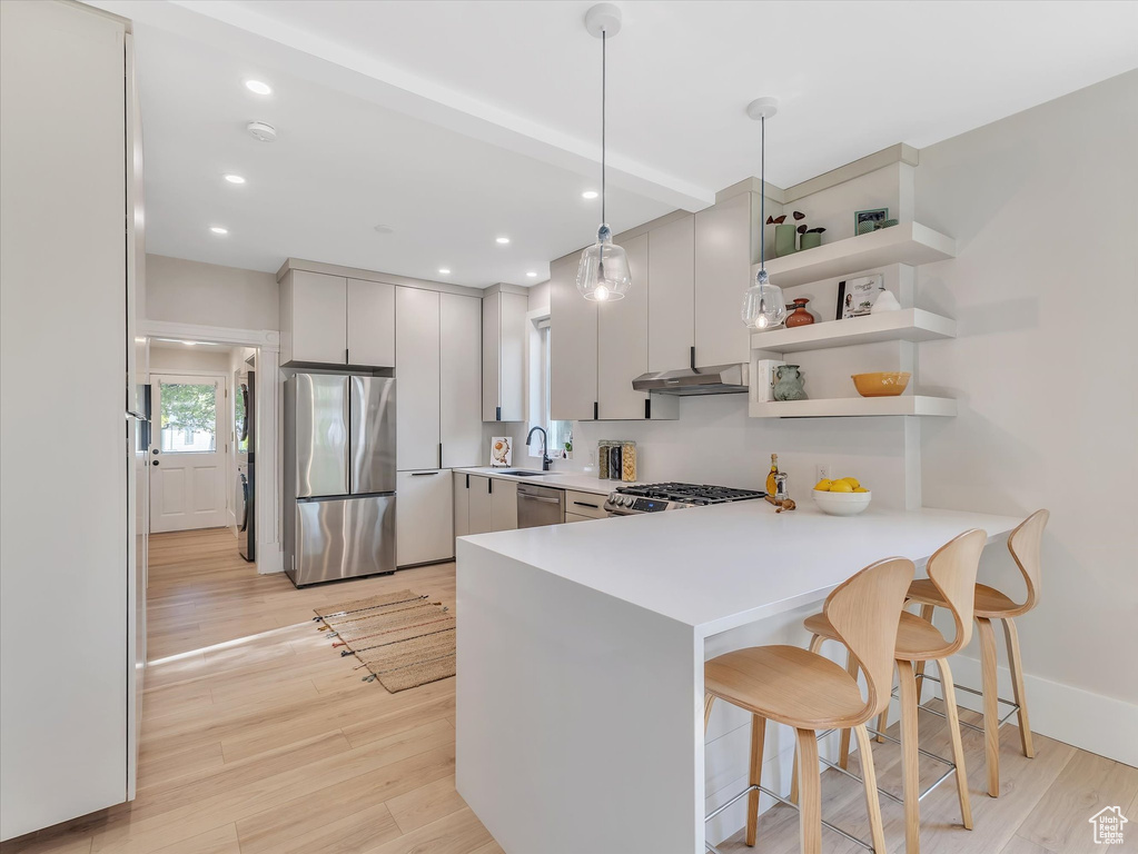Kitchen featuring decorative light fixtures, light hardwood / wood-style flooring, stainless steel appliances, and a breakfast bar