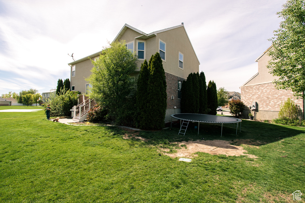 View of side of home with a trampoline and a yard