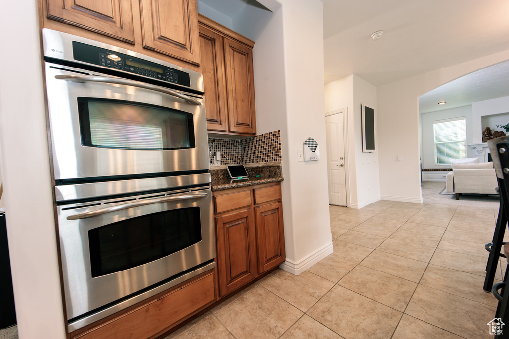 Kitchen with stainless steel double oven, dark stone countertops, tasteful backsplash, and light tile flooring