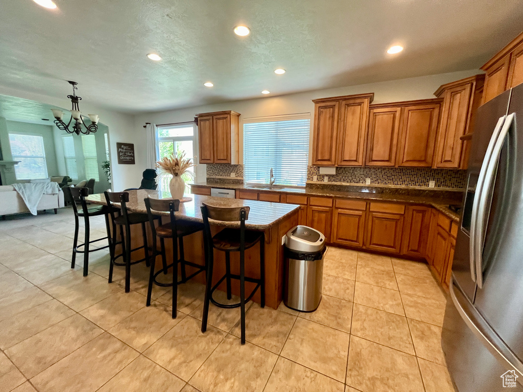 Kitchen with a kitchen island, stainless steel refrigerator with ice dispenser, tasteful backsplash, sink, and light tile floors