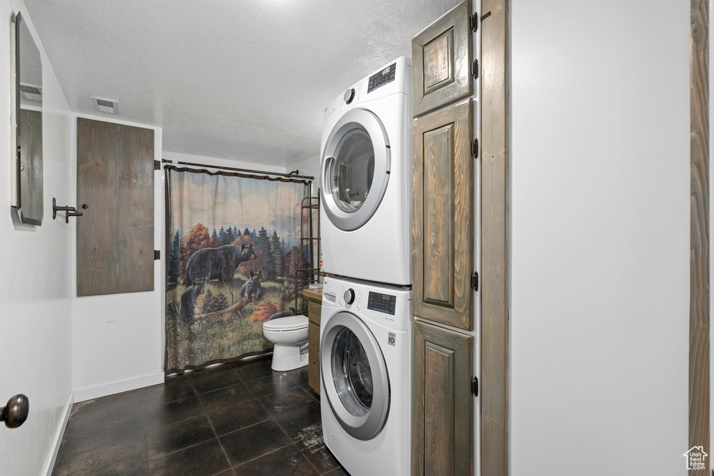 Laundry room with stacked washing maching and dryer and dark tile floors
