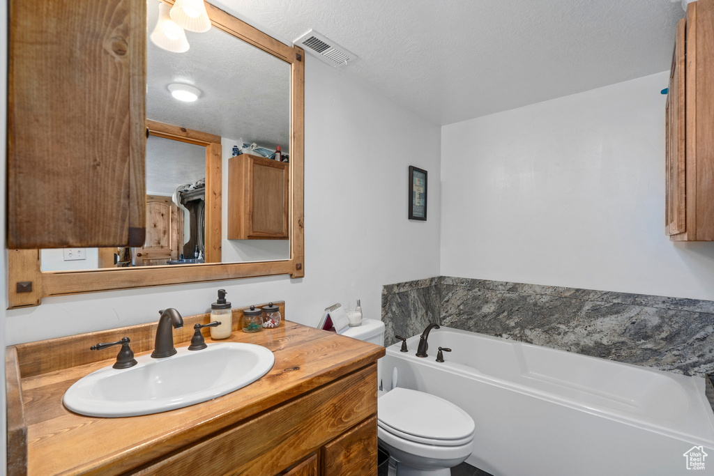 Bathroom with large vanity, toilet, a textured ceiling, and a tub