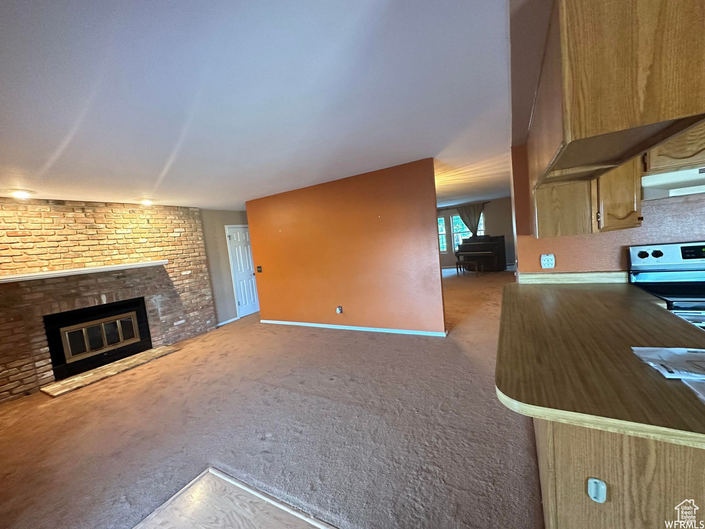 Unfurnished living room featuring carpet floors, brick wall, and a brick fireplace