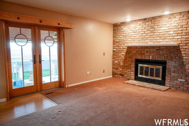 Unfurnished living room featuring a fireplace, french doors, and carpet