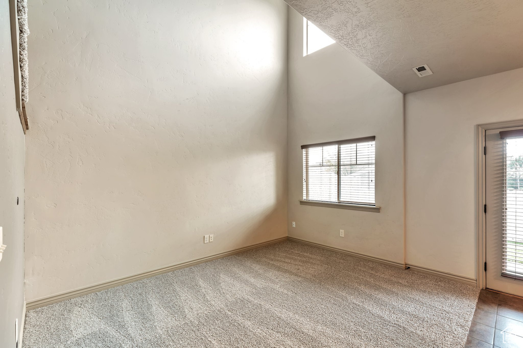 Carpeted spare room featuring a textured ceiling, a wealth of natural light, and vaulted ceiling