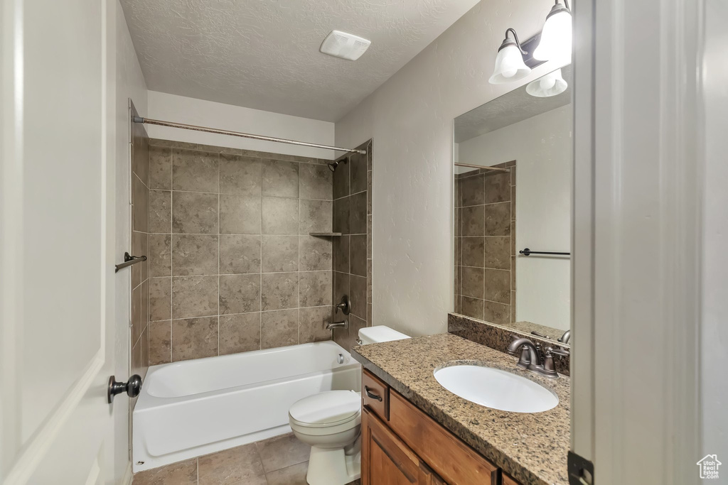 Full bathroom with tiled shower / bath, vanity, tile flooring, toilet, and a textured ceiling