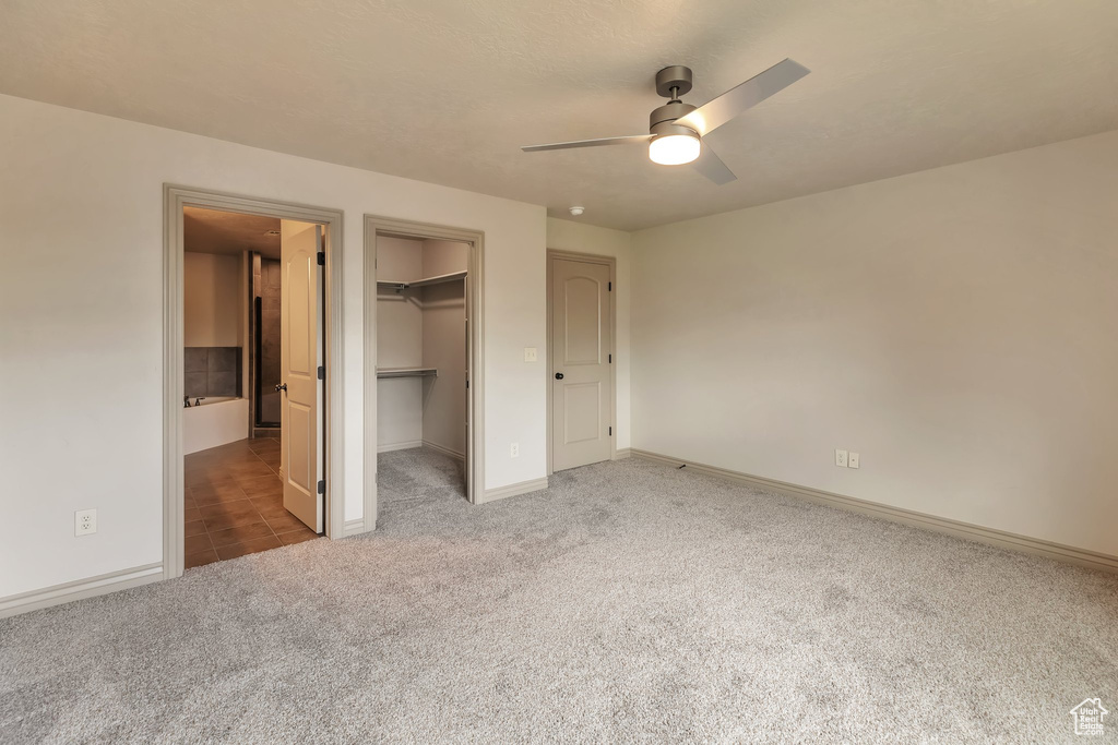 Unfurnished bedroom with a closet, ceiling fan, a walk in closet, and dark tile floors