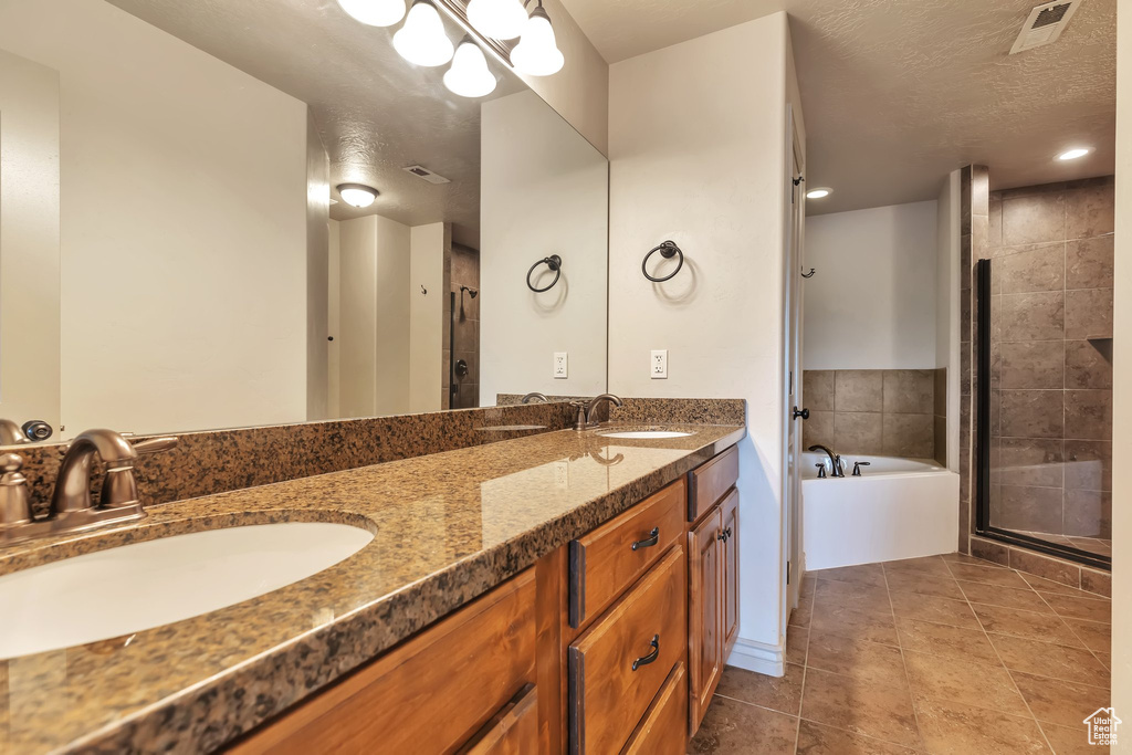 Bathroom featuring a textured ceiling, plus walk in shower, tile floors, and double vanity