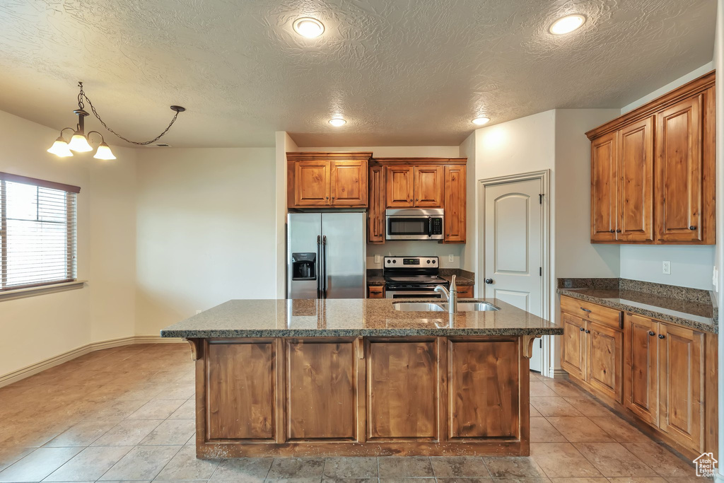 Kitchen featuring light tile floors, sink, decorative light fixtures, stainless steel appliances, and a center island with sink