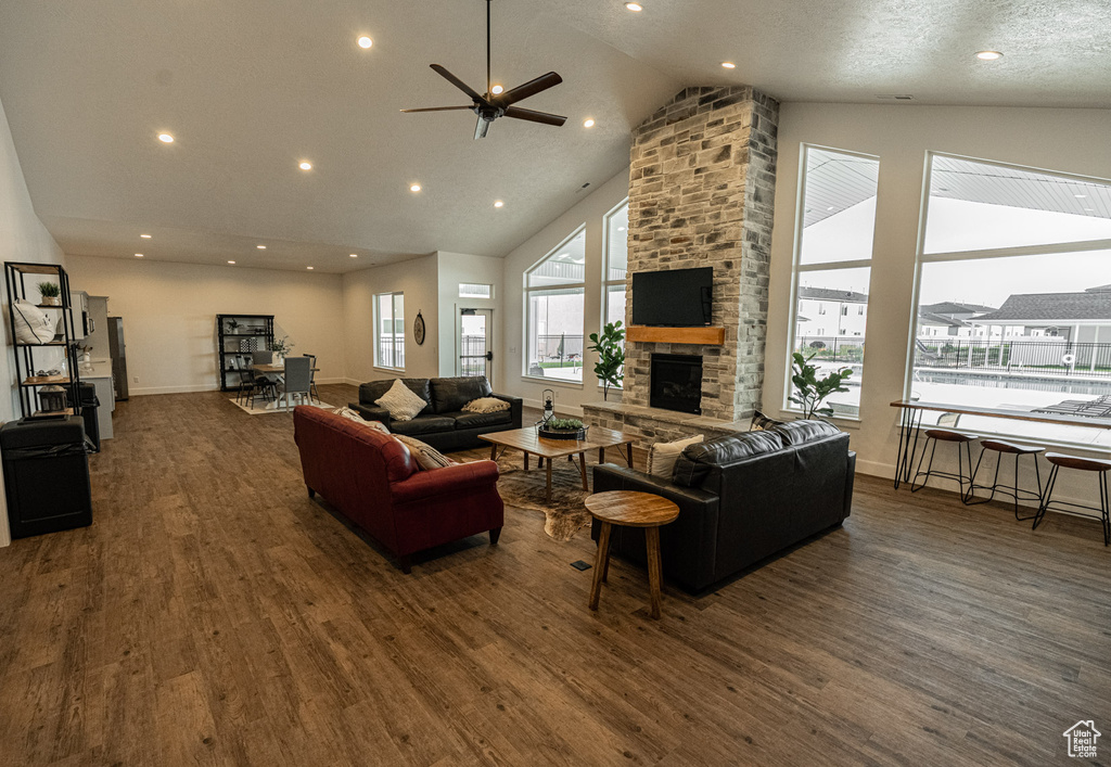 Living room featuring high vaulted ceiling, ceiling fan, a stone fireplace, and dark hardwood / wood-style floors