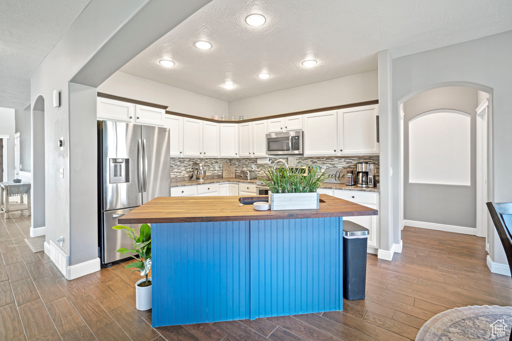 Kitchen featuring white cabinets, butcher block countertops, stainless steel appliances, and a center island