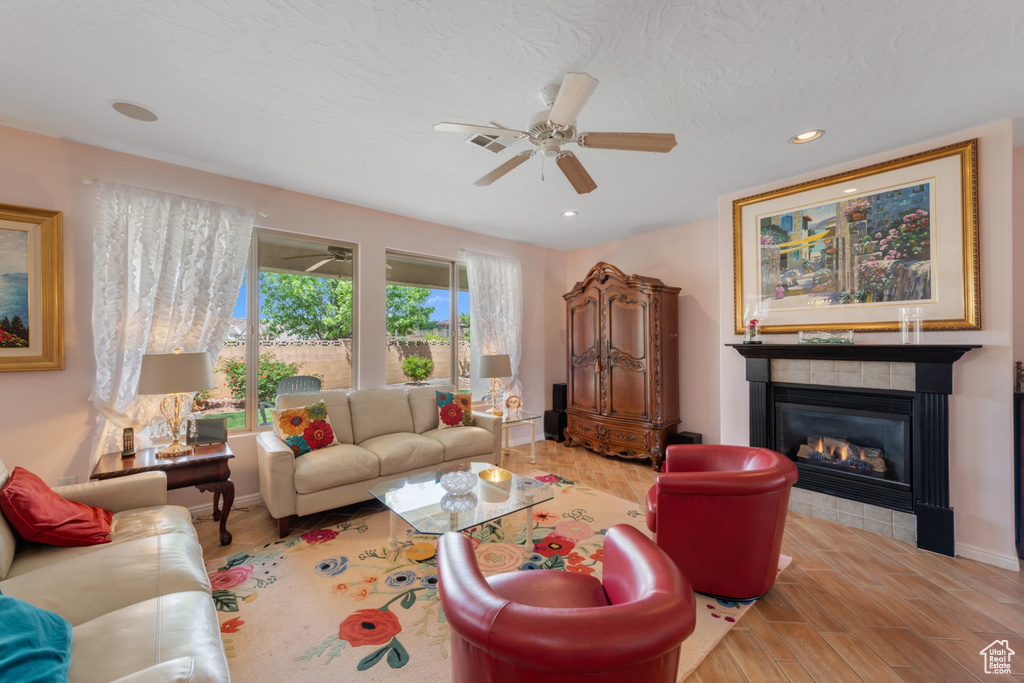 Living room featuring ceiling fan, light hardwood / wood-style flooring, and a tiled fireplace