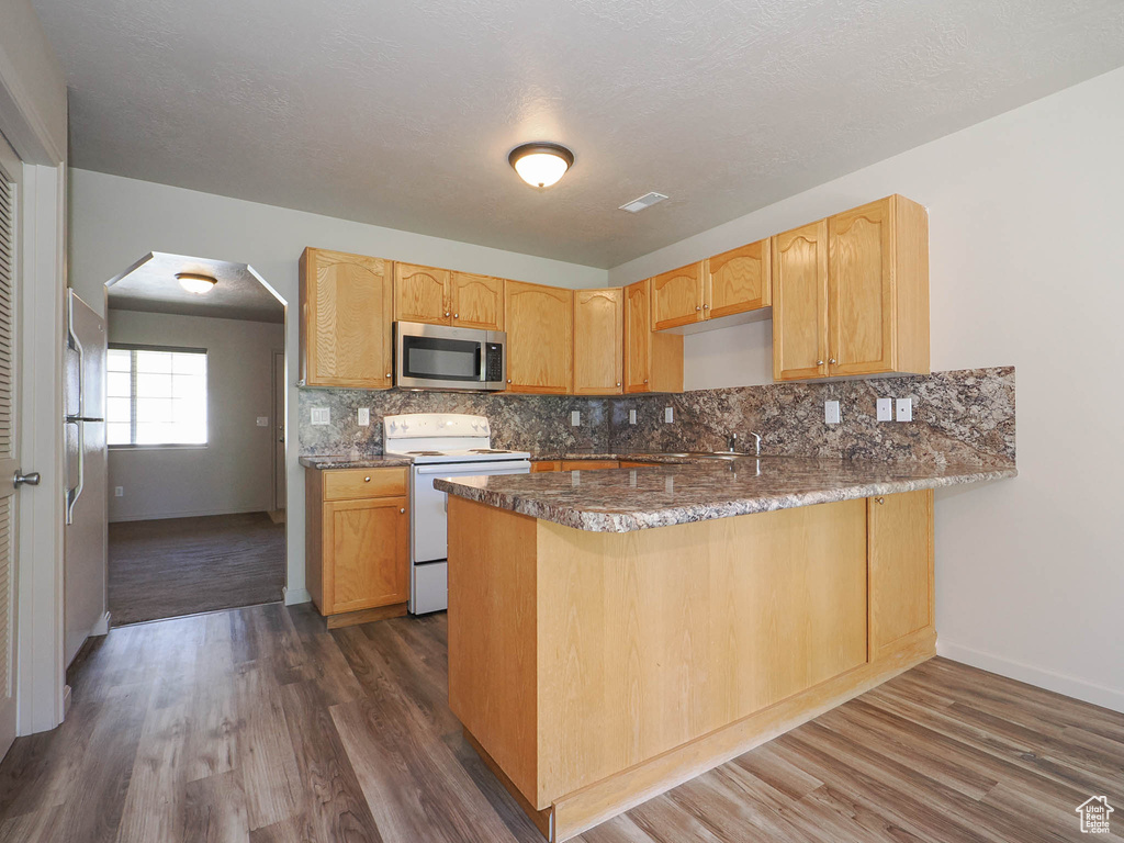 Kitchen with light brown cabinets, tasteful backsplash, white electric stove, dark wood-type flooring, and kitchen peninsula
