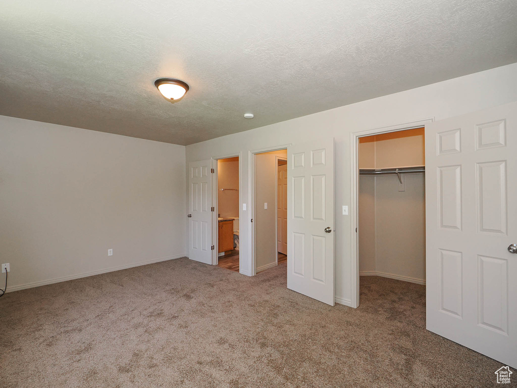 Unfurnished bedroom featuring carpet flooring, a textured ceiling, a closet, and a walk in closet