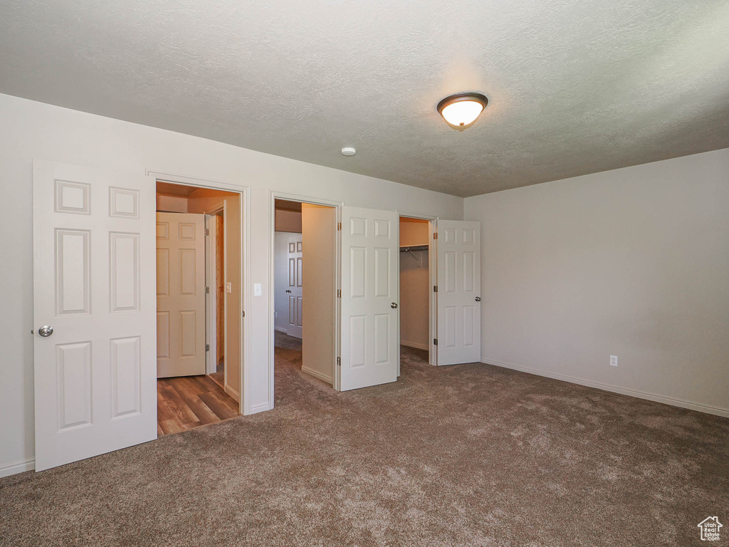 Unfurnished bedroom featuring a walk in closet, dark carpet, a closet, and a textured ceiling