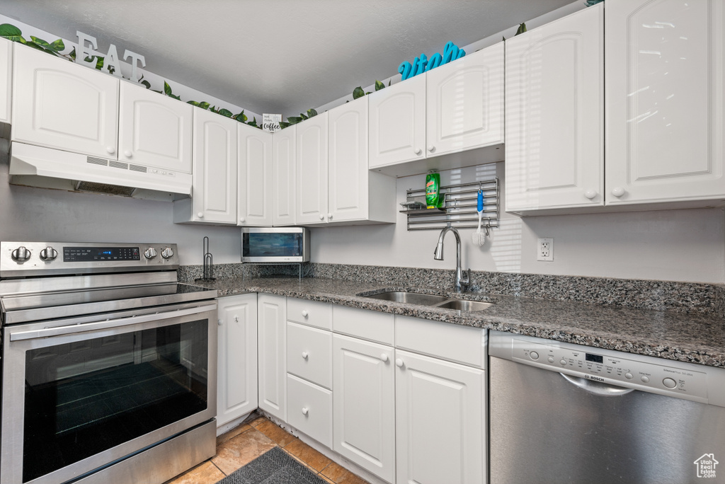 Kitchen with appliances with stainless steel finishes, white cabinets, sink, and light tile flooring