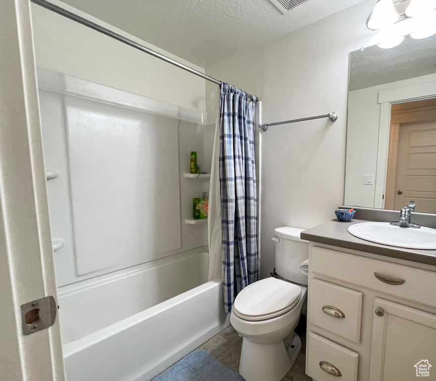 Full bathroom with vanity with extensive cabinet space, shower / bath combo with shower curtain, a textured ceiling, tile floors, and toilet