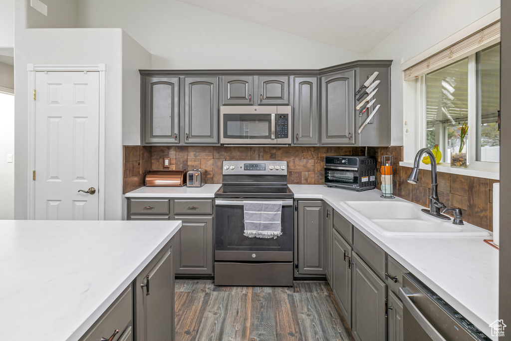 Kitchen featuring sink, backsplash, dark wood-type flooring, lofted ceiling, and stainless steel appliances