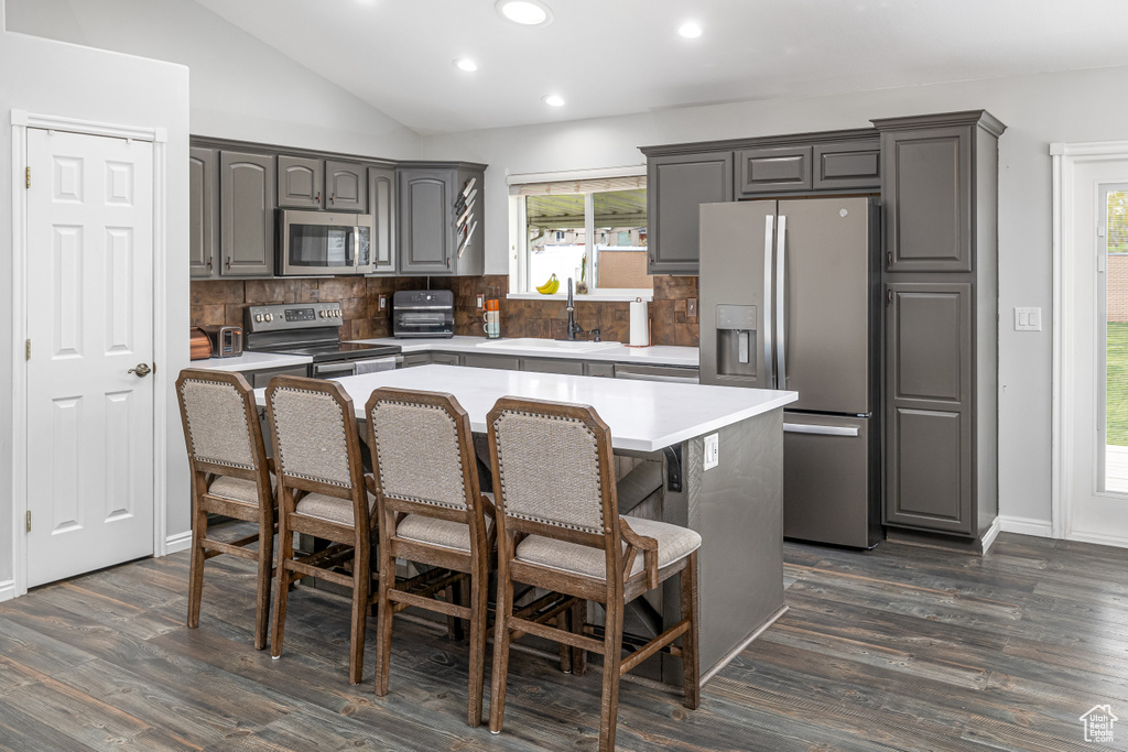 Kitchen featuring a center island, dark hardwood / wood-style floors, backsplash, appliances with stainless steel finishes, and lofted ceiling