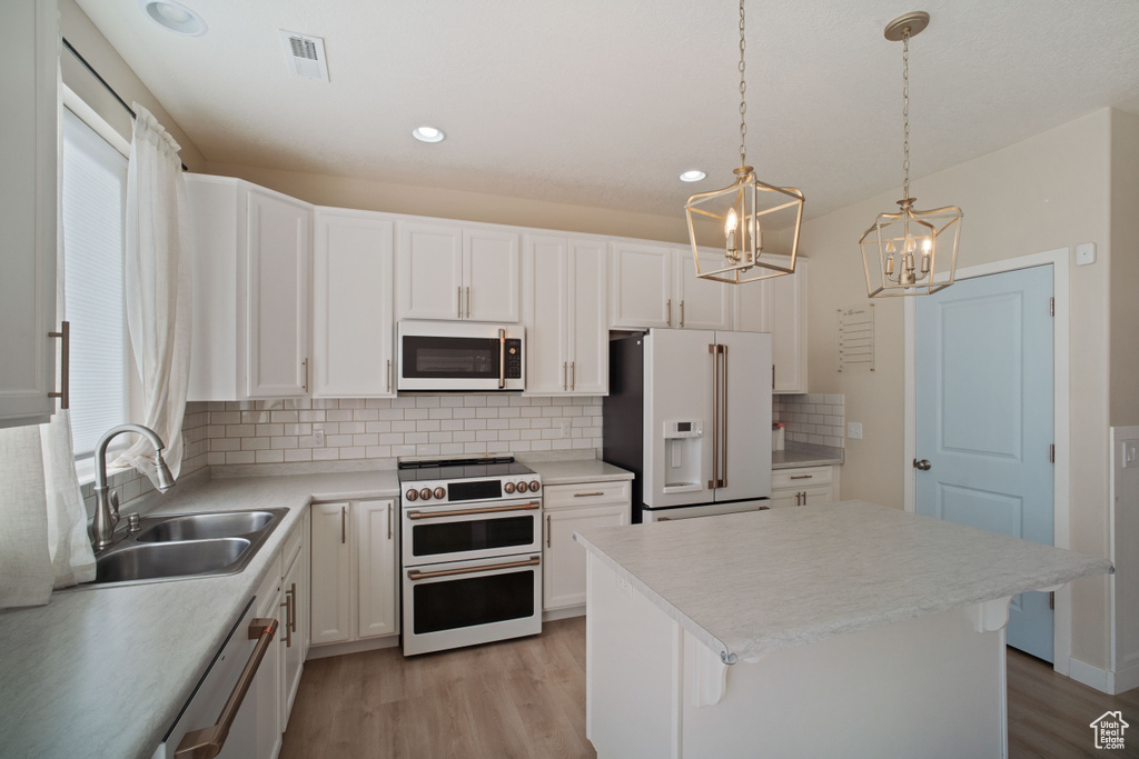 Kitchen featuring a kitchen island, premium appliances, tasteful backsplash, hanging light fixtures, and light hardwood / wood-style flooring