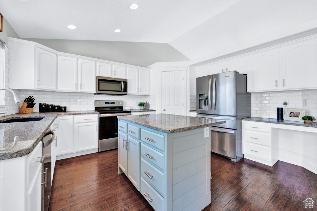 Kitchen featuring appliances with stainless steel finishes, a kitchen island, sink, backsplash, and lofted ceiling