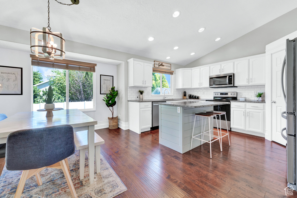 Kitchen with a center island, white cabinets, dark wood-type flooring, backsplash, and stainless steel appliances