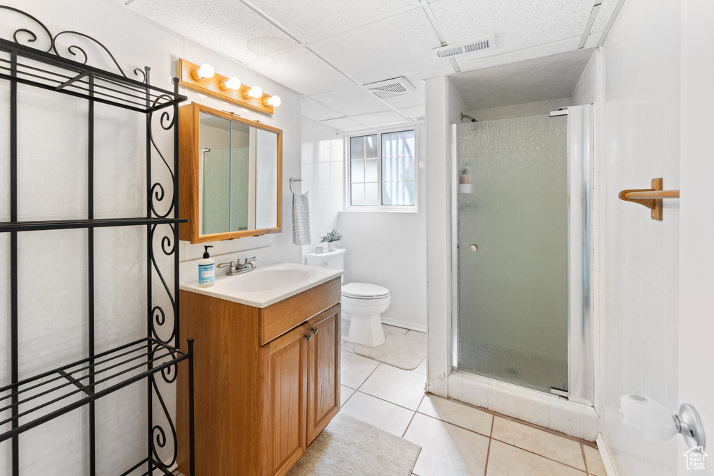Bathroom featuring tile flooring, a paneled ceiling, oversized vanity, walk in shower, and toilet