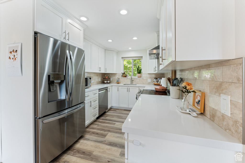 Kitchen with white cabinets, sink, light hardwood / wood-style floors, backsplash, and stainless steel appliances