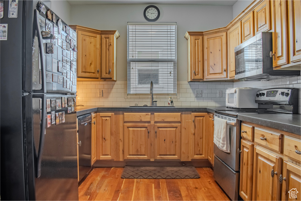 Kitchen with light hardwood / wood-style flooring, tasteful backsplash, sink, and black appliances