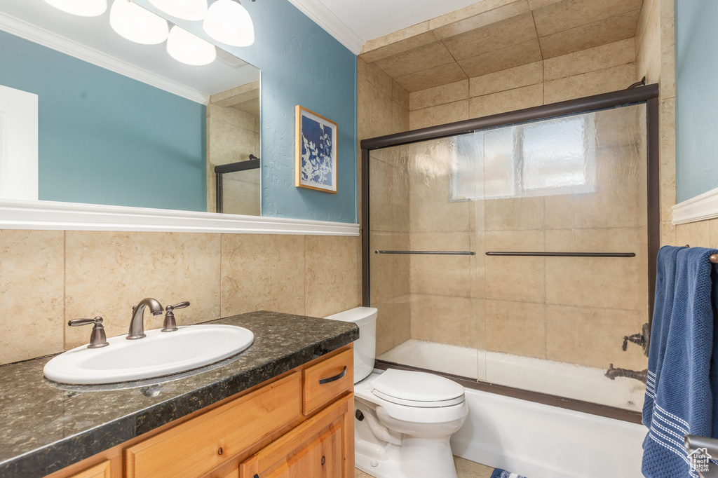 Full bathroom with vanity, tile walls, backsplash, enclosed tub / shower combo, and toilet