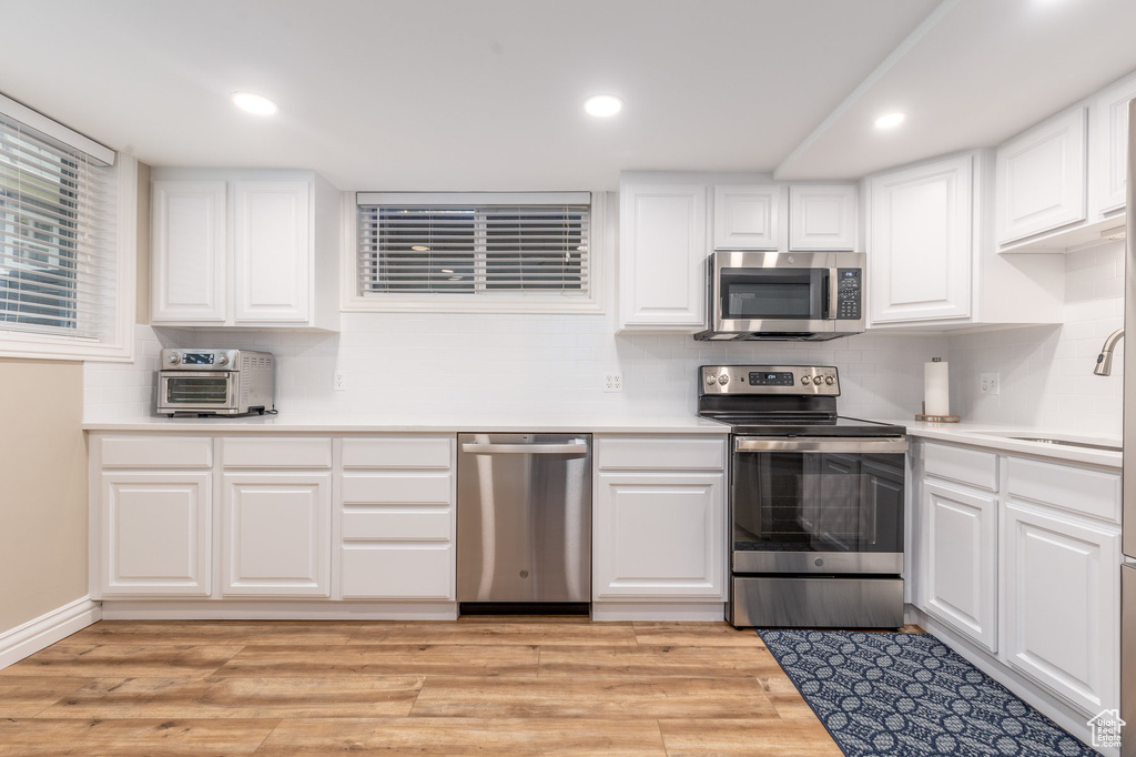 Kitchen with appliances with stainless steel finishes, sink, light hardwood / wood-style floors, tasteful backsplash, and white cabinetry