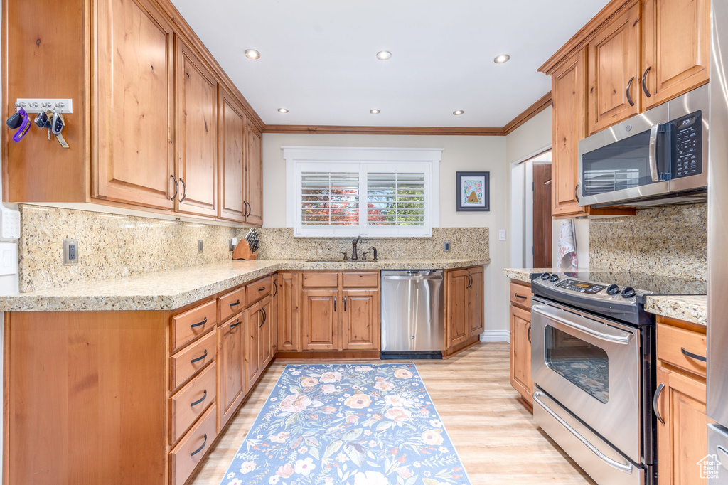 Kitchen featuring backsplash, light stone countertops, stainless steel appliances, and light hardwood / wood-style floors