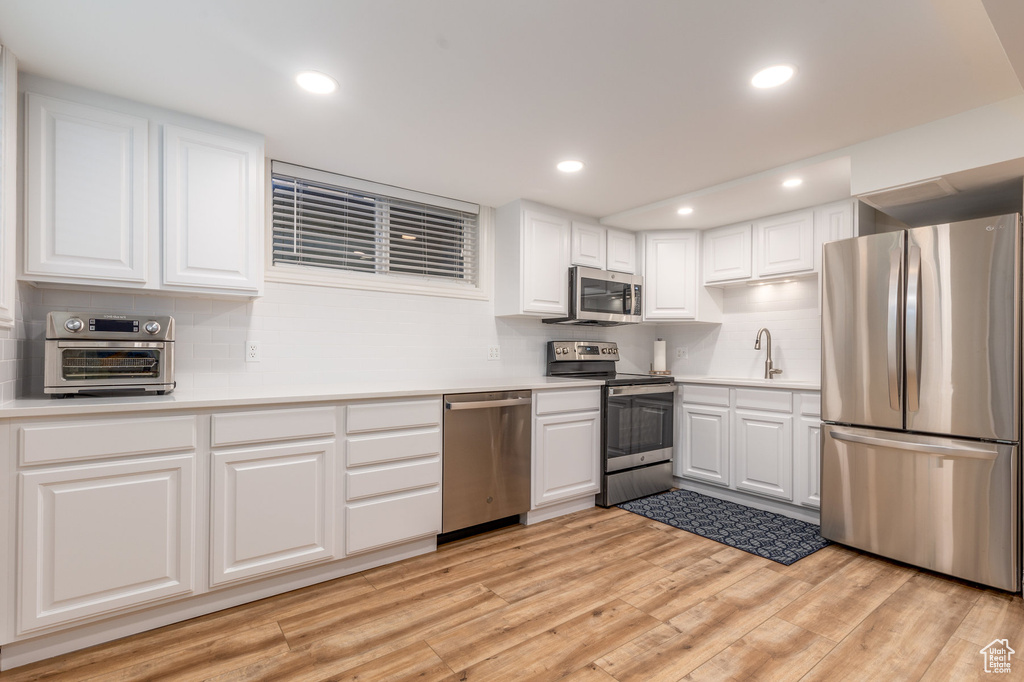 Kitchen featuring backsplash, stainless steel appliances, white cabinetry, sink, and light wood-type flooring