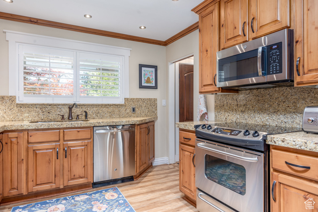 Kitchen with appliances with stainless steel finishes, tasteful backsplash, light hardwood / wood-style floors, and sink