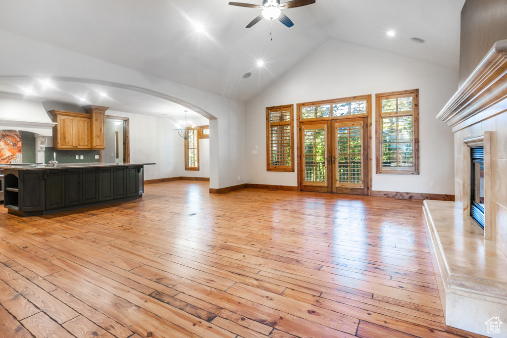 Unfurnished living room featuring high vaulted ceiling, light hardwood / wood-style floors, and ceiling fan with notable chandelier