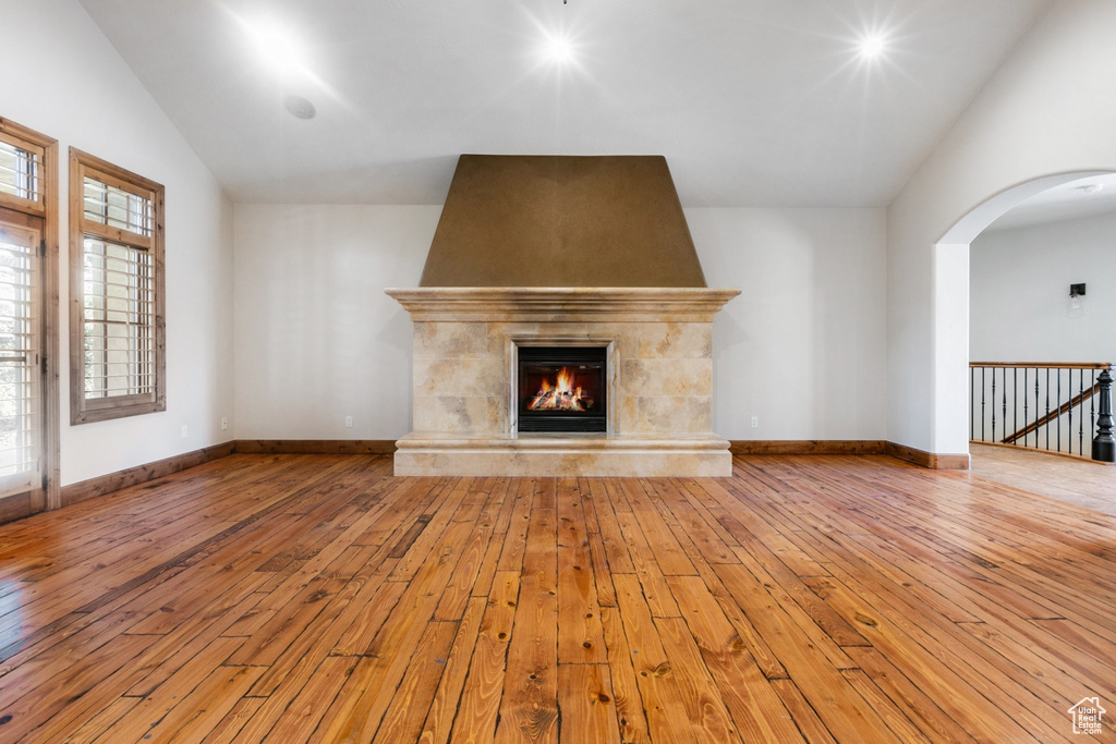 Unfurnished living room with a wealth of natural light, a tile fireplace, lofted ceiling, and light hardwood / wood-style flooring