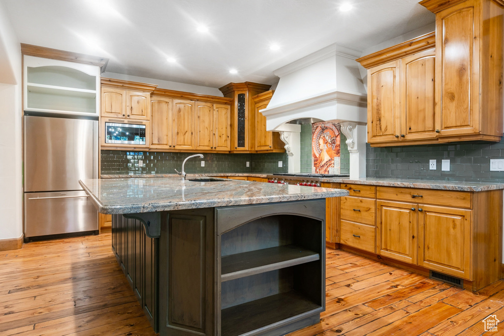 Kitchen featuring appliances with stainless steel finishes, light hardwood / wood-style flooring, tasteful backsplash, and an island with sink