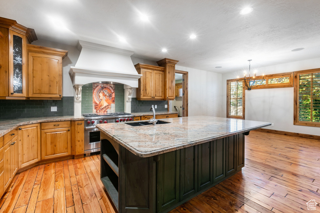 Kitchen with range with two ovens, tasteful backsplash, an island with sink, and custom exhaust hood