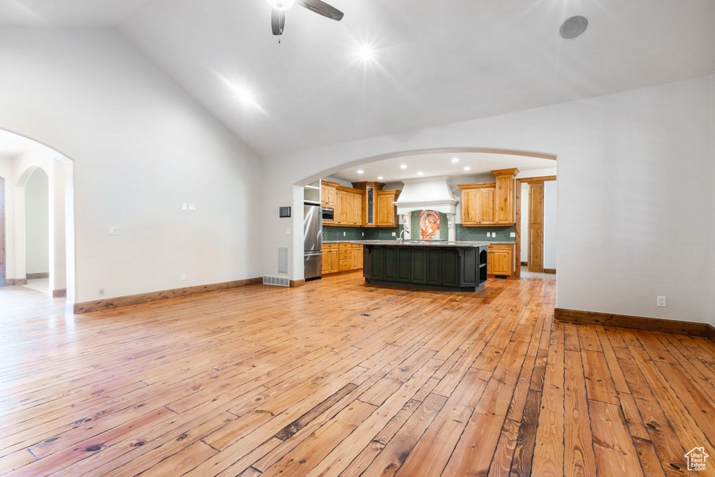 Unfurnished living room with light hardwood / wood-style flooring, ceiling fan, sink, and high vaulted ceiling