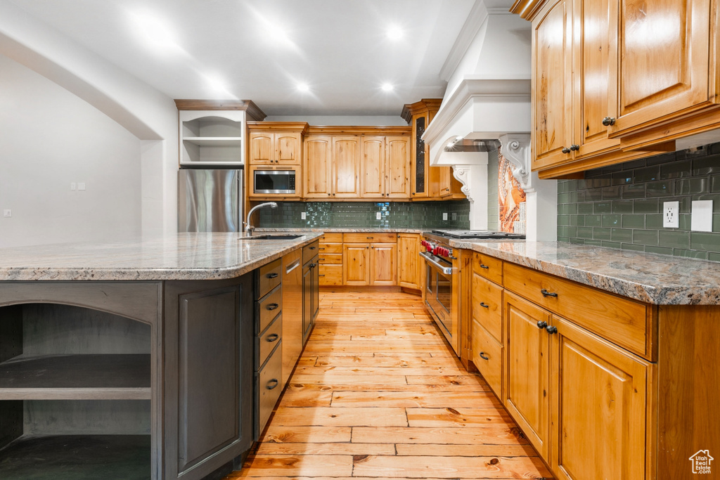 Kitchen with custom range hood, light wood-type flooring, tasteful backsplash, stainless steel appliances, and sink