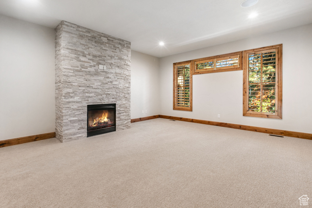 Unfurnished living room with plenty of natural light, light carpet, and a stone fireplace