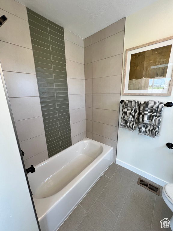 Bathroom featuring toilet, tile flooring, tiled shower / bath combo, and a textured ceiling