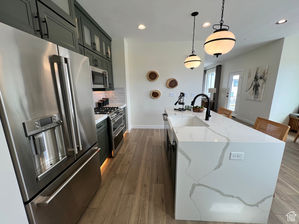 Kitchen with wood-type flooring, hanging light fixtures, sink, high quality appliances, and tasteful backsplash