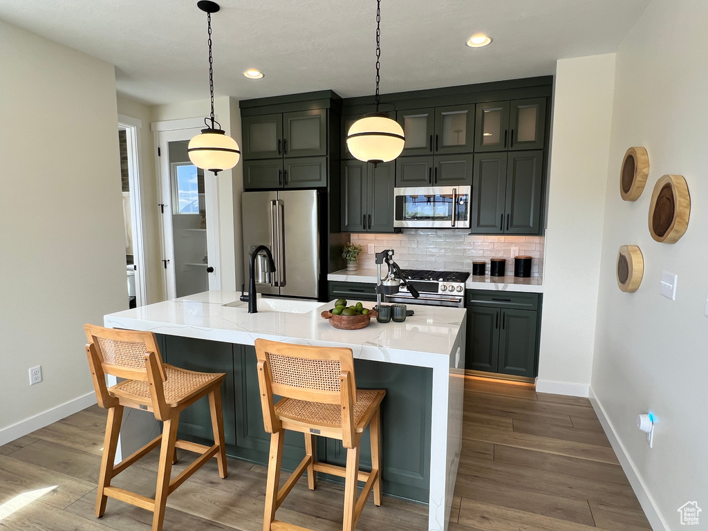 Kitchen featuring stainless steel appliances, decorative light fixtures, hardwood / wood-style flooring, and a center island with sink